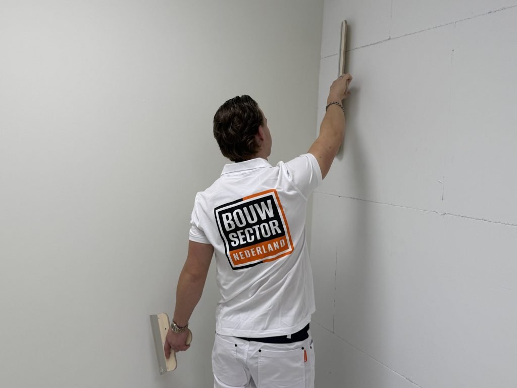 Stukadoor strekt zijn arm en haalt de spaan langs de bovenrand van een wand in een hoek