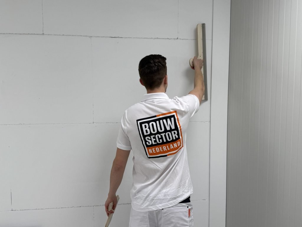 Stukadoor met het logo van Bouwsector Nederland op zijn rug werkt een wand bovenaan glad