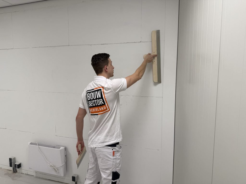 Stukadoor controleert met een lange spaan of een lichte wand overal vlak is