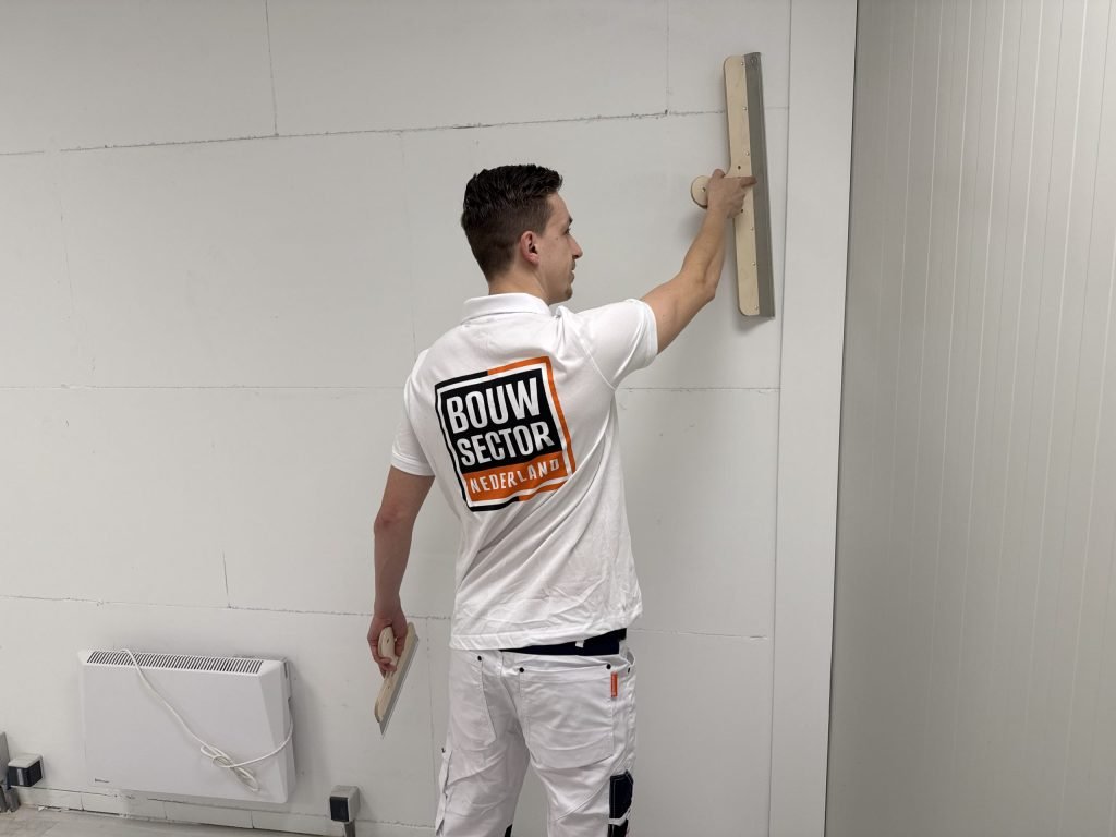 Stukadoor van Bouwsector Nederland kijkt langs de spaan terwijl hij een wand vlak zet