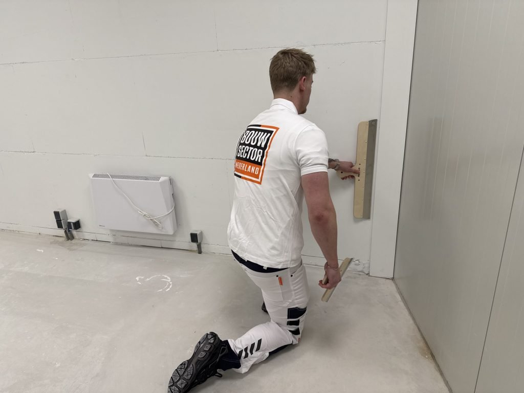 Stukadoor zit op een knie en haalt de spaan langs het onderste deel van een wand bij de hoek