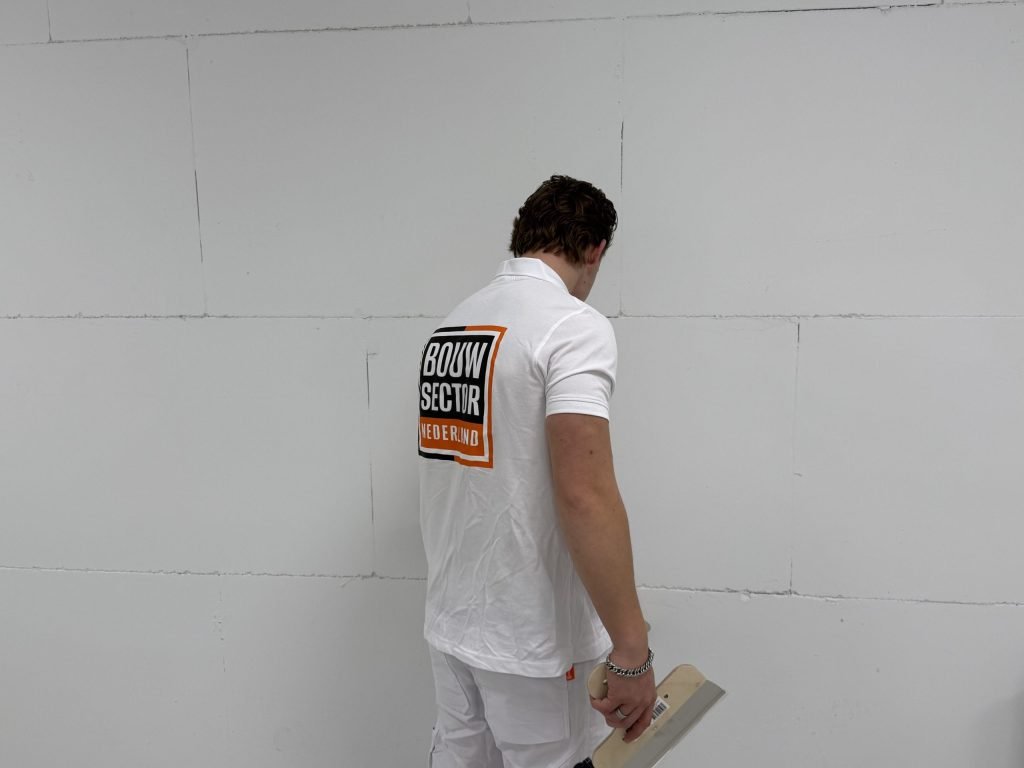 Stukadoor van Bouwsector Nederland bekijkt een kale wand met plaatnaden, een plakspaan in de hand
